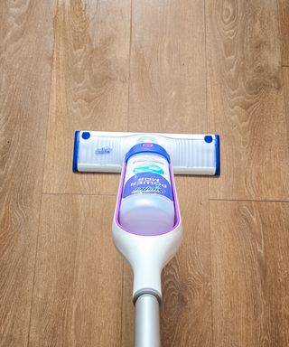 A Swiffer PowerMop with a white base with purple trim, on a wooden vinyl floor