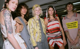 Models wear white top and skirt, striped blazer and brown top, yellow jacket and grey dress, red and white striped jumpsuit, and pink polo shirt
