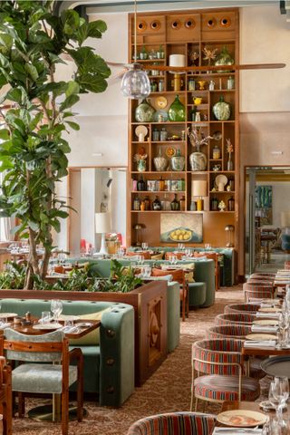 A vibrantly decorated restaurants features an earthy palette of greens, browns, and reds, all reflected in the mid-century modern plush decor ranging from soft banquettes and chairs to colossal bookcases in wood.