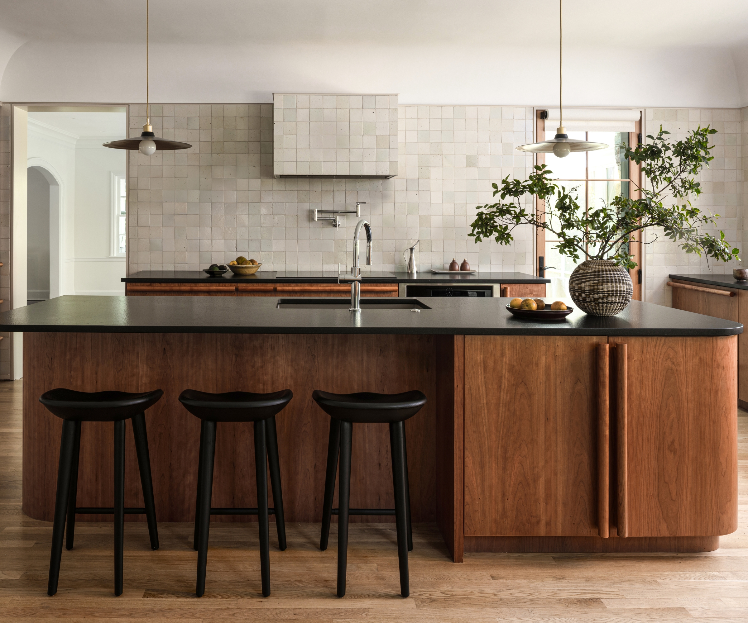 A large kitchen with a cherry wood island and cabinetry, black countertops, and neutral wall tiles