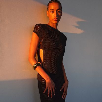 Model stood in golden hour sunlight wearing a black crochet dress with a chunky silver bangle sold at Harvey Nichols