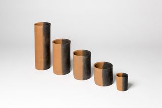 5 Clay vessels of different height featuring 2 sides - one half black, one half orange photographed against a grey background