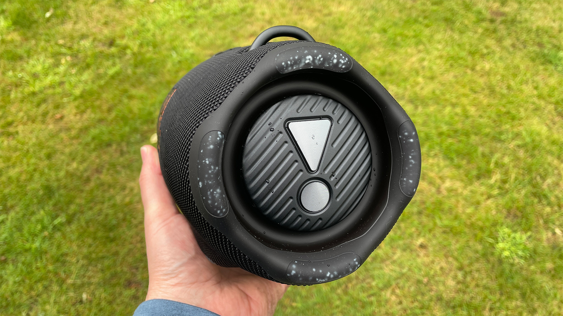 The end of a black JBL Xtreme 4 wireless speaker. A grassy lawn is visible in the background.