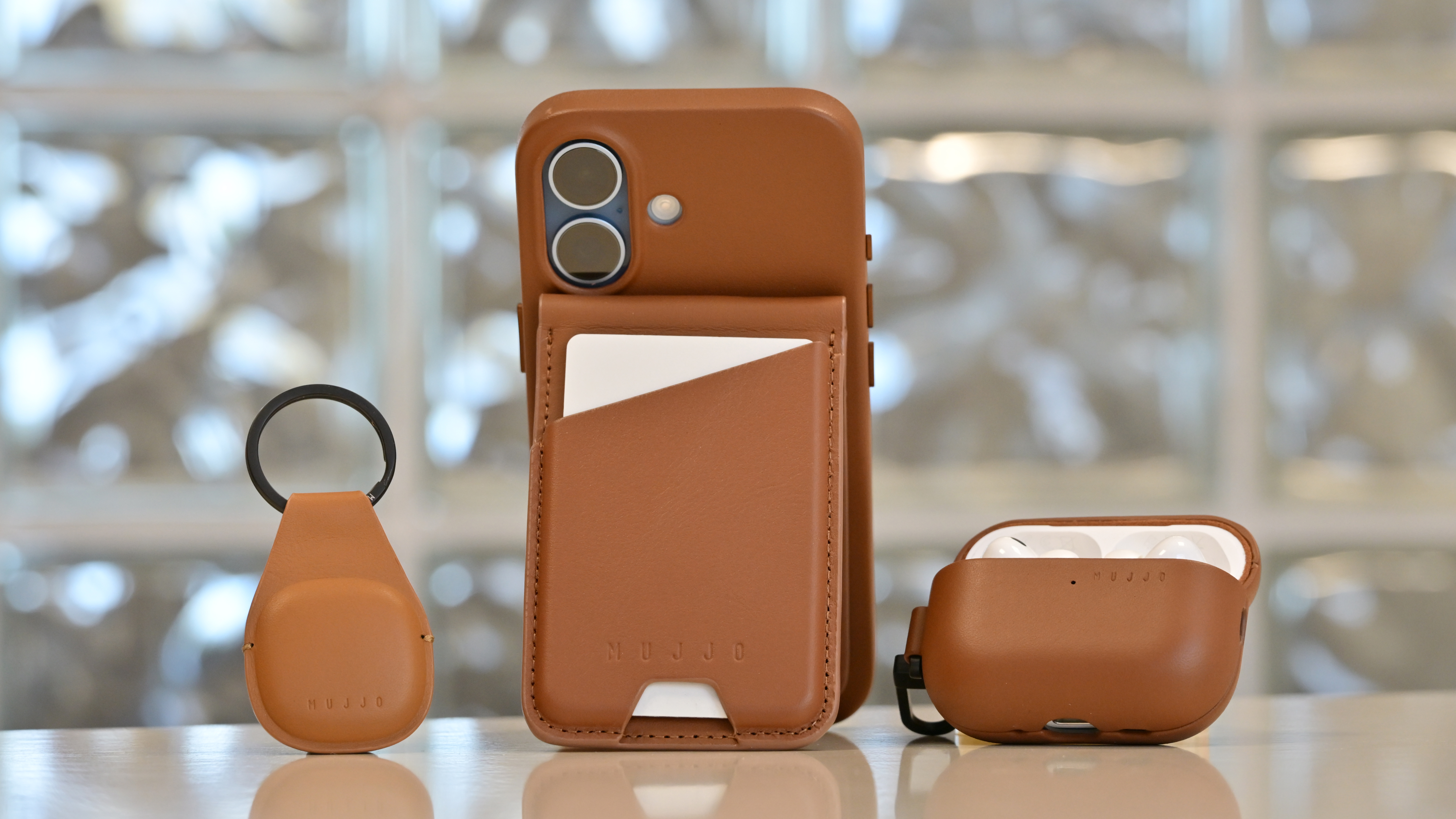 Mujjo Full Leather Case for iPhone 17 with leather kickstand, alongside AirPods case and AirTag keyfob
