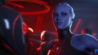 A blue-skinned woman with crest-like head tendrils and facial markings stands in a dimly lit, red-toned room wearing a dark, high-collared outfit.