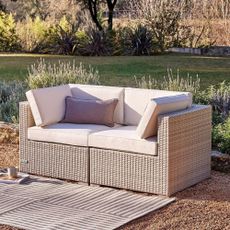 A rattan garden sofa with white cushions and an outdoor rug
