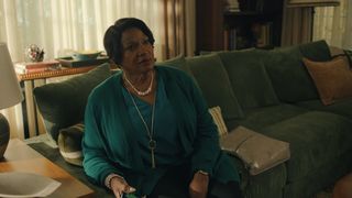 Anna Maria Horsford wearing a green cardigan sitting on a green couch in a home in the netflix show no good deed