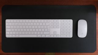 Apple keyboard and mouse in white on a black leather mat on a wooden desk