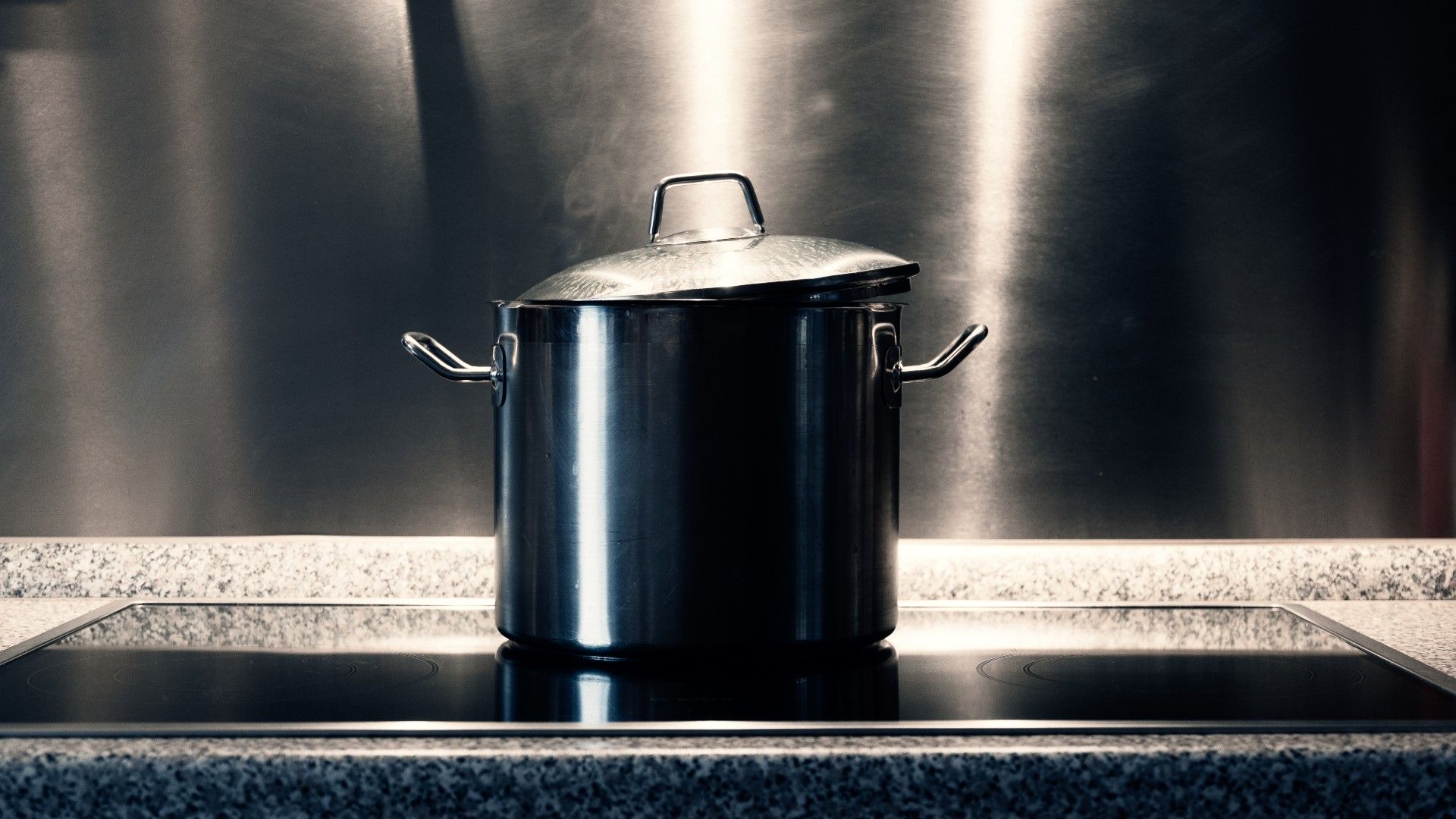 large stainless steel pot on a hob, with stainless steel backsplash
