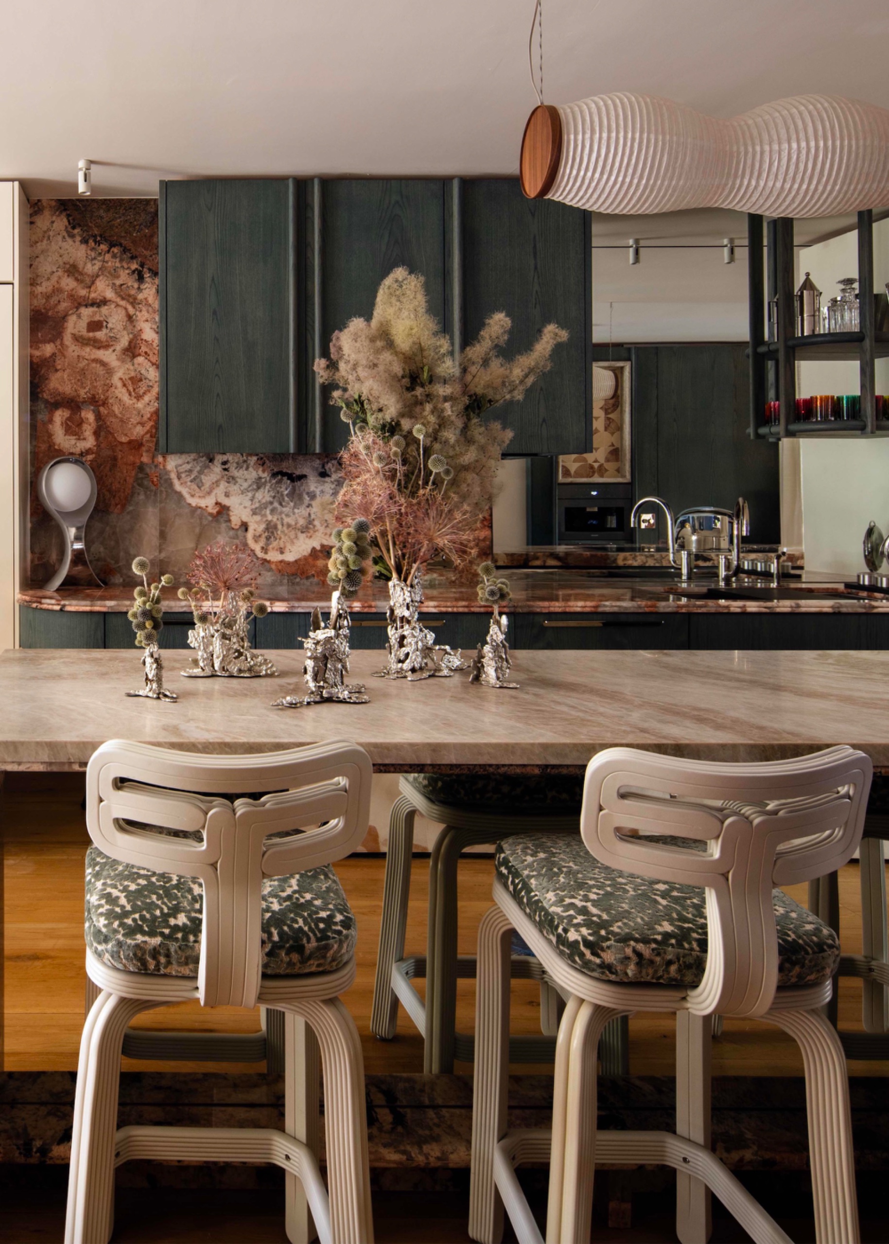 Dark blue-green stained oak kitchen cabinetry with richly veined Patagonia quartzite, pale stone island and sculptural white chairs.