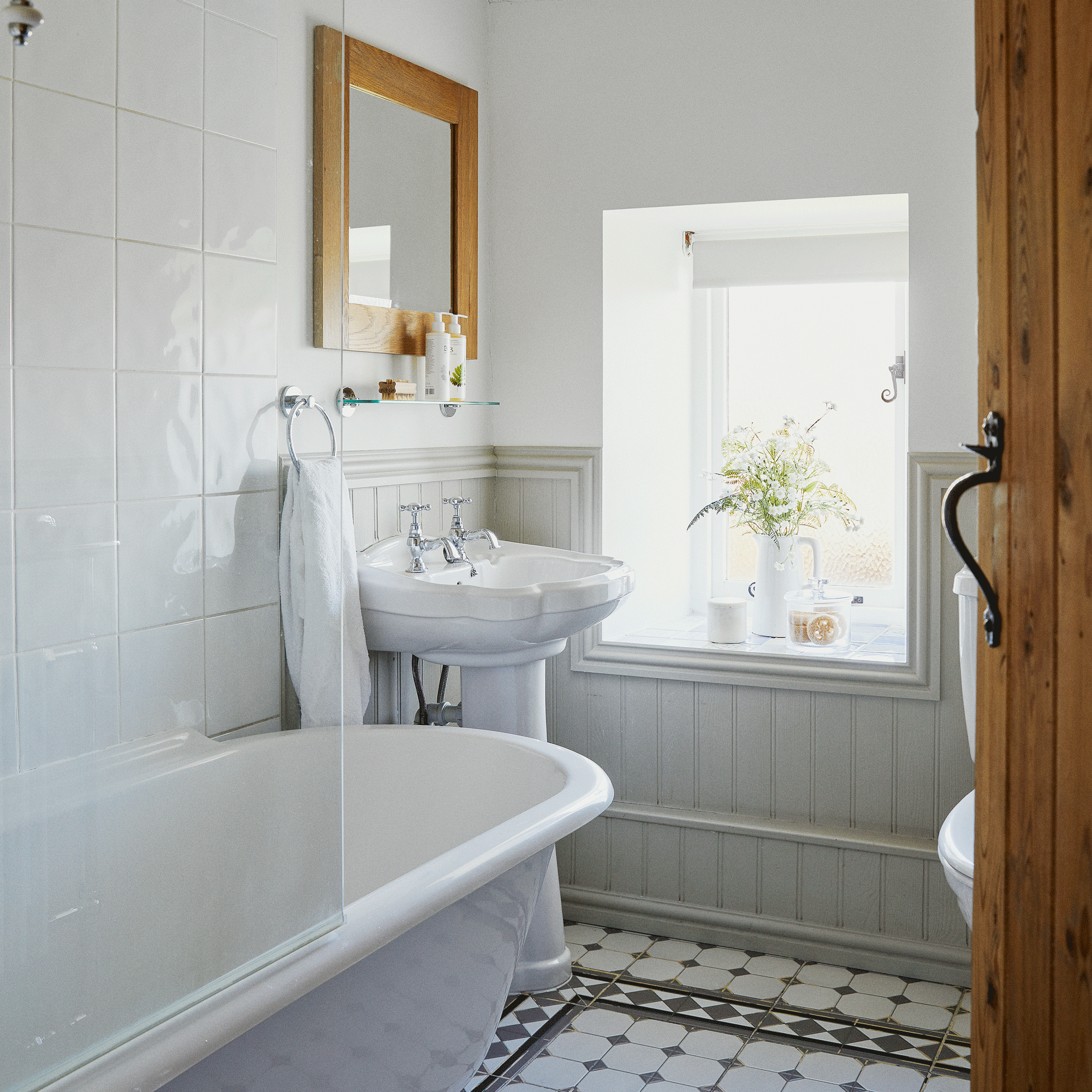 a white bathroom with wood cladding and tiles on the walls, a shower bath and black and white tiled floor