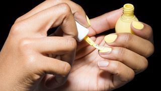 A woman's hand painting her nails yellow