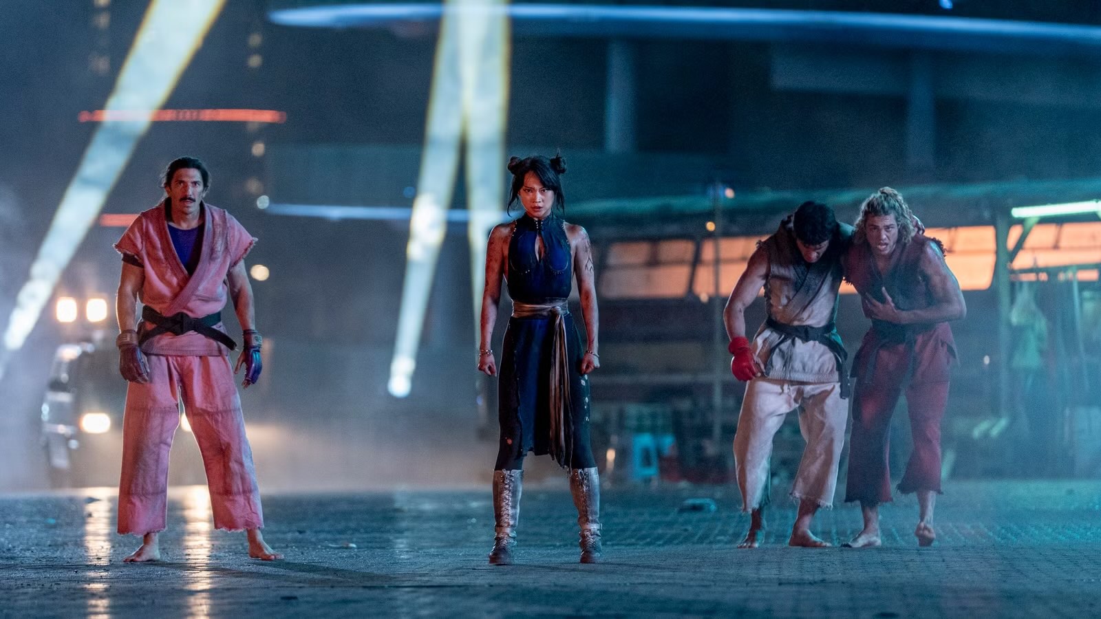 the cast of street fighter looks battered in uniform after a fight standing on top of a building at night in a still from the movie