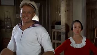Robin Williams dressed as Popeye, looking mean, standing next to Shelly Duvall as Olive Oyl.