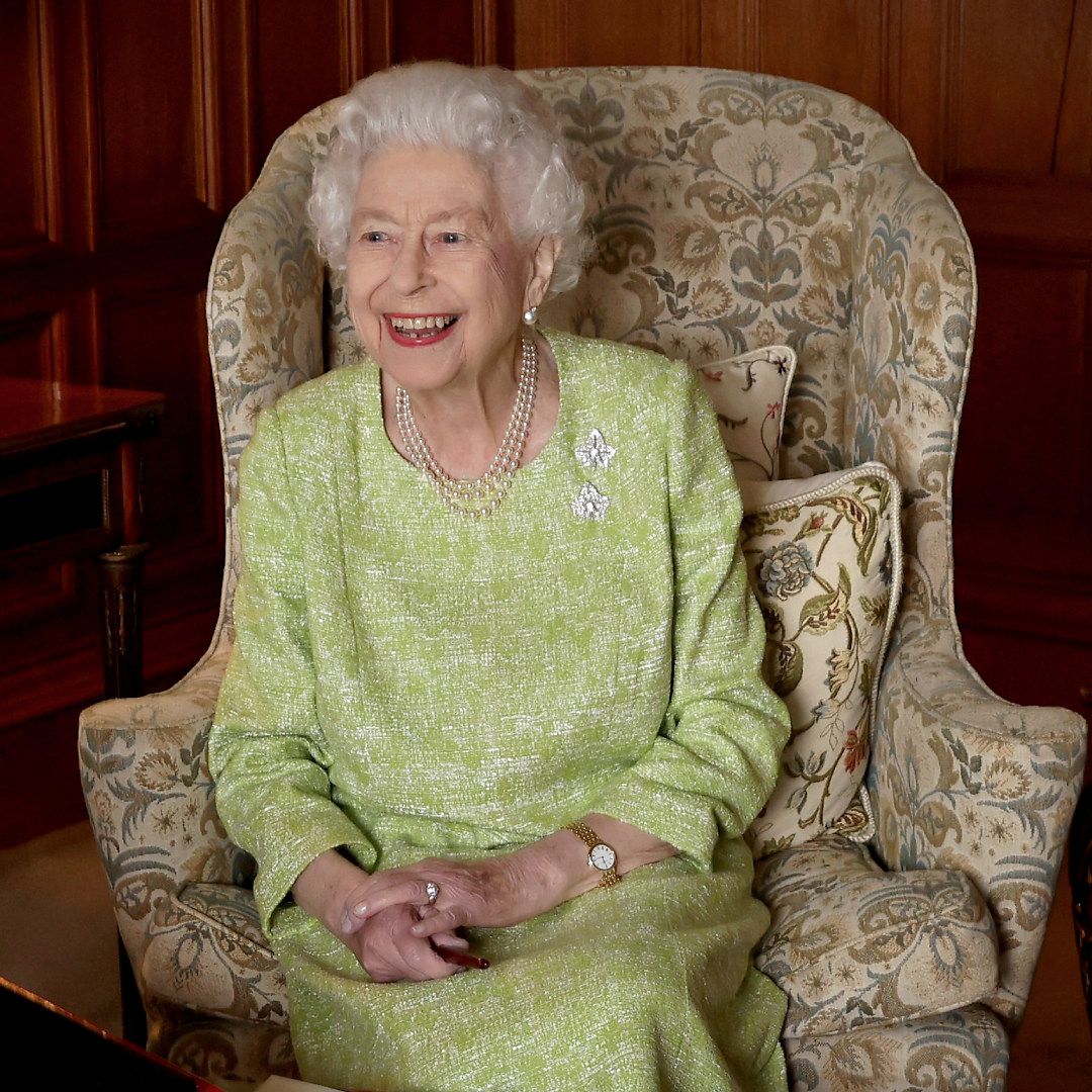 Queen Elizabeth sitting in a chair in a green dress and laughing