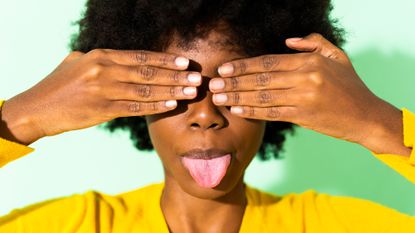 Woman sticks her tongue out and covers her eyes