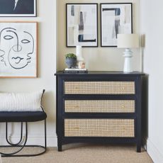 Biege painted bedroom with a black chest of drawers with rattan frontage, with decor on top it and artwork on the wall