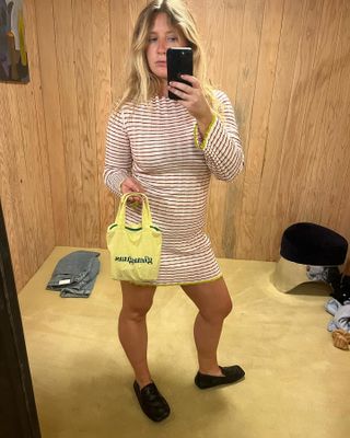 Influencer Martine Lavelle poses for a mirror selfie wearing a Guest in Residence striped dress, mini yellow Gimaguas tote bag, and black loafers.