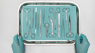 Person holding tray with surgical equipment against a white background.
