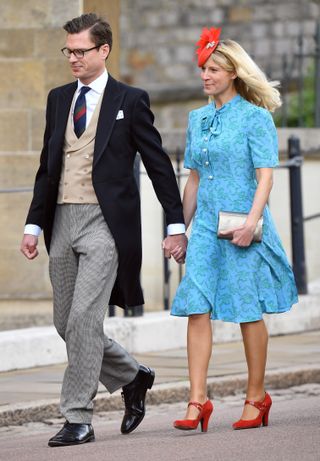 Lady Rose Gilman wearing a blue dress and red heels with a red hat holding hands with husband George Gilman in a morning suit walking outside