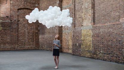 A cloud of white balloons hovers over a woman.