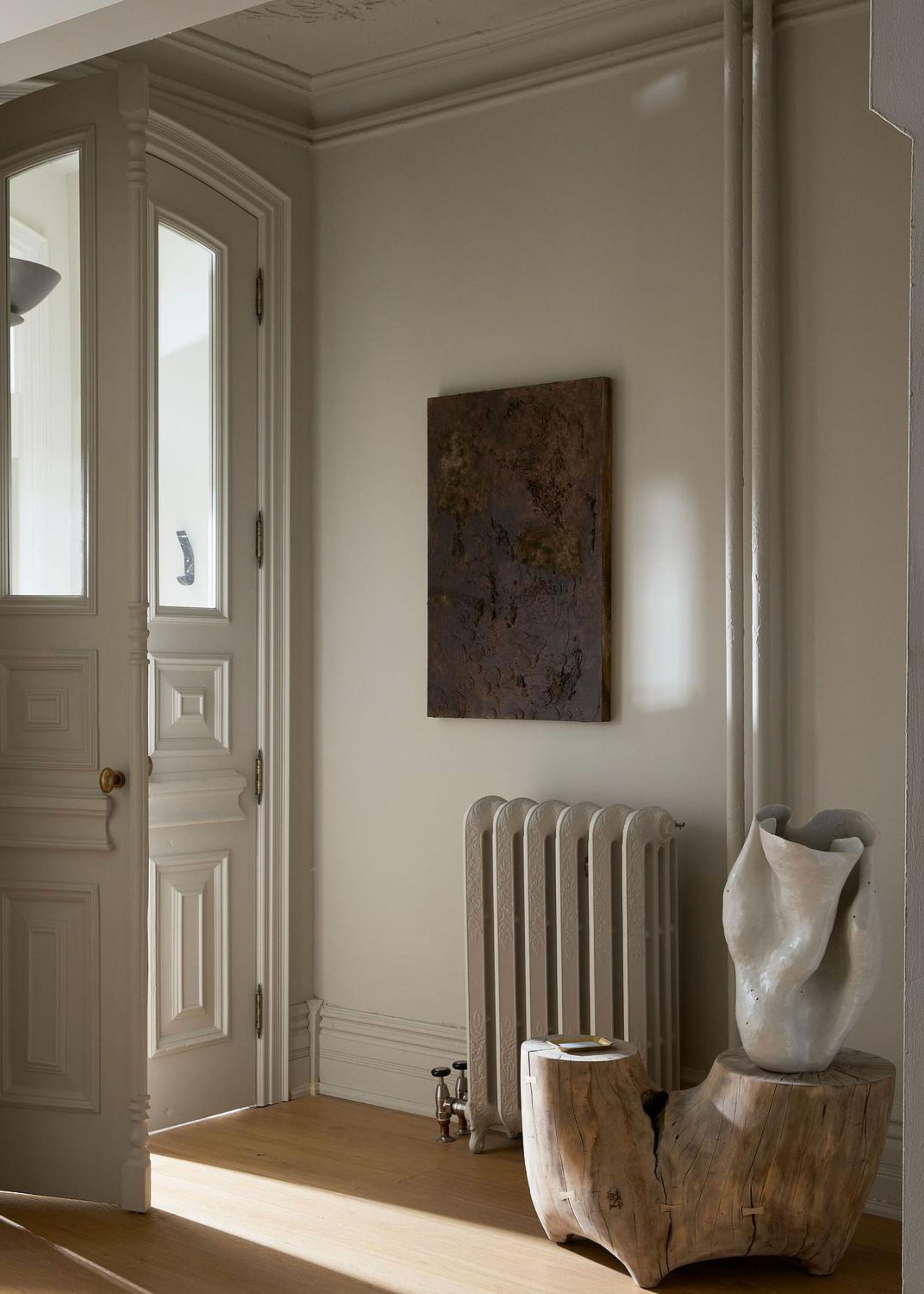 An entryway of a home with a radiator and a piece of art hanging above it. Beside the radiator is a seating area as well as a vase on top of it