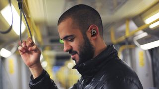En mand står i en bus med Creative Outlier Pro i ørerne