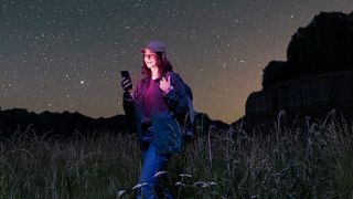 Woman looking at her smartphone as she hikes in the wilderness underneath a starry sky