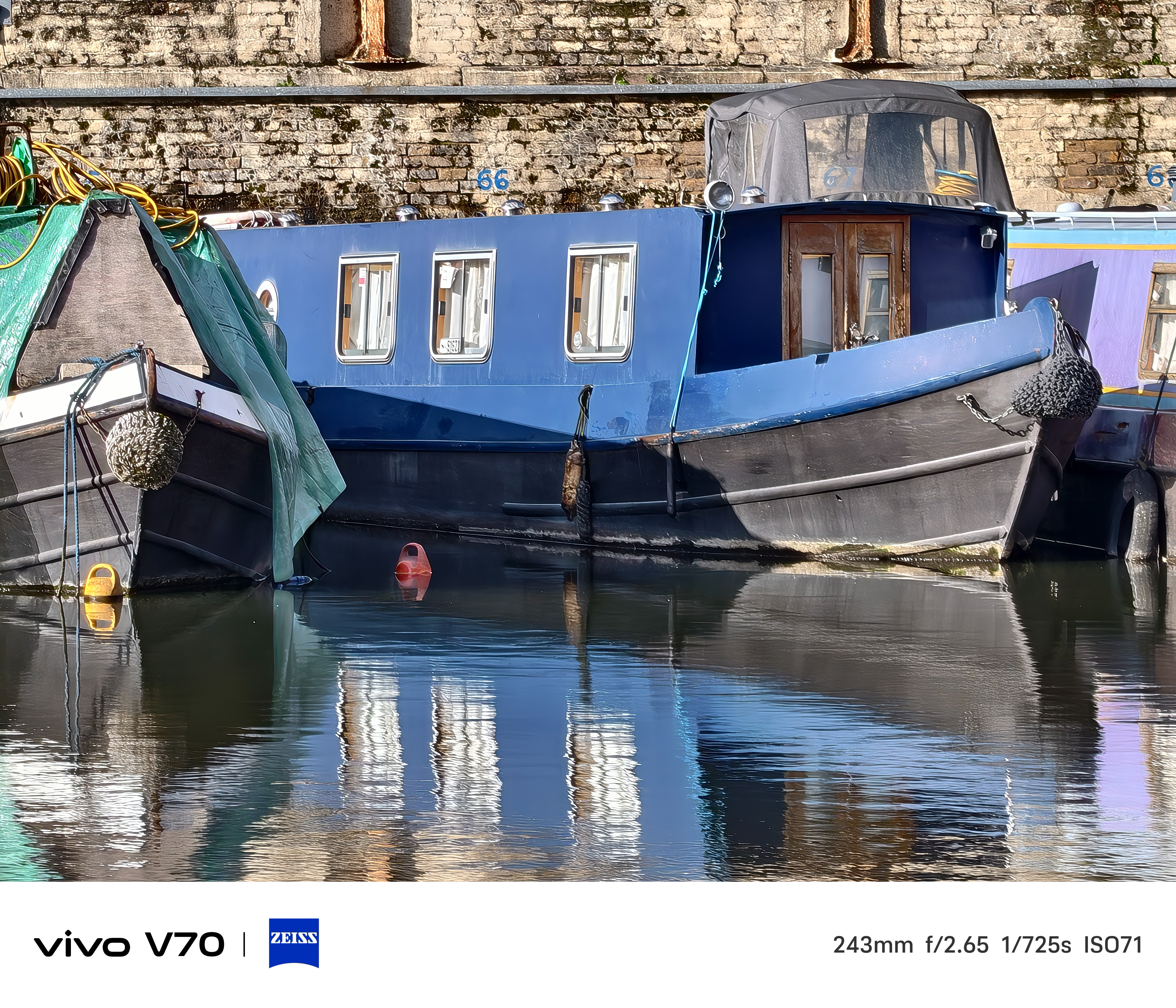 Close-up of blue narrowboat moored on canal with strong reflections in calm water.