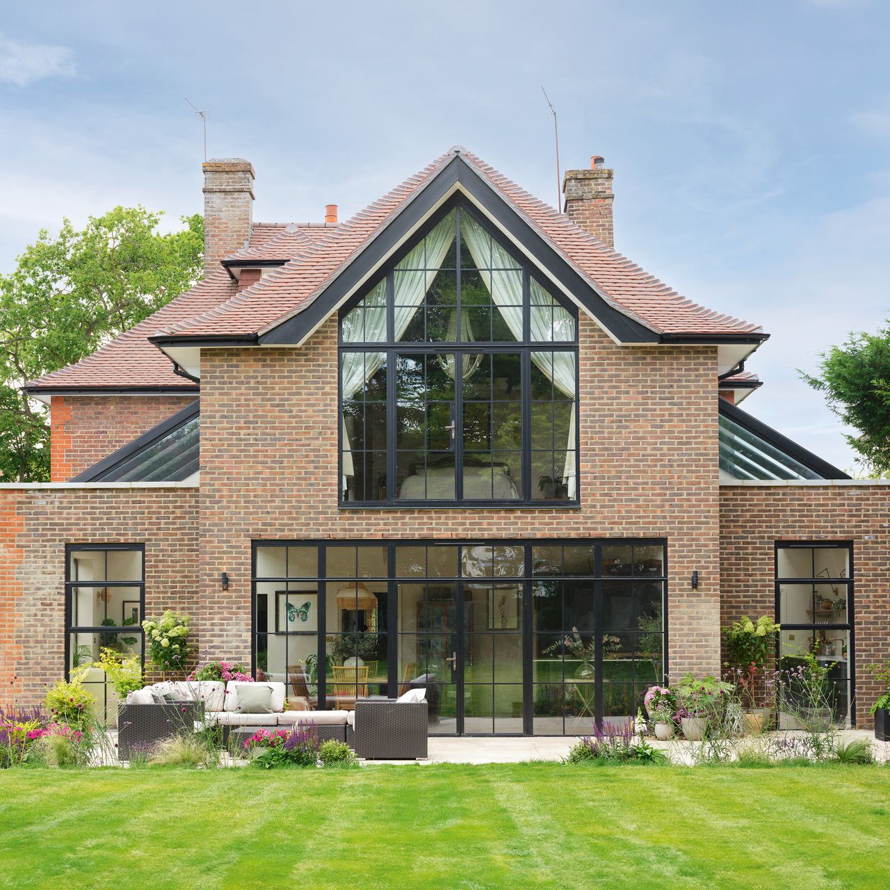 exterior of a property with large statement glazing and large patio doors that open out into a well-kept patio and garden
