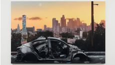 Photograph of destroyed car against backdrop of city skyline at sunset, from Sayre Gomez ‘Heaven ‘N‘ Earth’ exhibition at Xavier Hufkens
