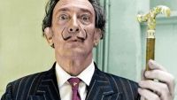 A man in a thin moustache holds up a gold cane