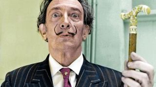 A man in a thin moustache holds up a gold cane