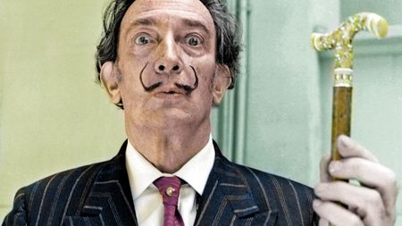 A man in a thin moustache holds up a gold cane