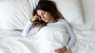 A woman with long brown hair sleeps on a white mattress