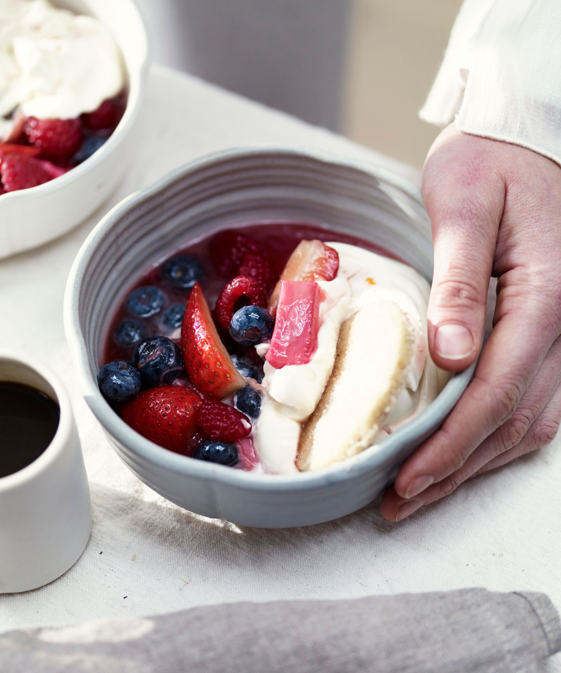 Summer fruit compote with syllabub in a small dish held in a hand