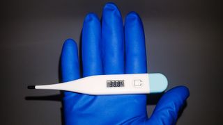 a gloved hand holds a thermometer