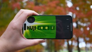 A hand holding up an iPhone with the Huji Cam disposable camera app on the screen