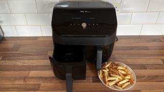 The Instant Vortex Plus Dual Drawer Air Fryer with one basket partially removed and a plate of chips cooked in the air fryer next to it