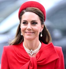 Kate Middleton wearing a red coat and headband walking next to Prince William wearing a blue suit on Commonwealth Day 2025