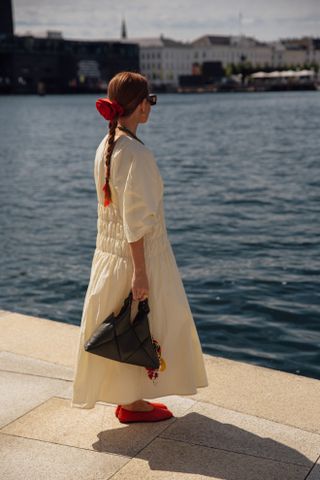 a woman at Copenhagen Fashion Week wearing a cream dress and a black bag with a red rosette clip from Pico Store