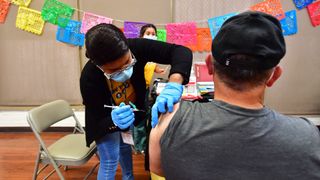 A woman wearing blue latex gloves administering a vaccine to a man