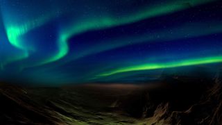 An artist's impression of the new sinuous discrete aurora over Mars. There are green wavy lines of light against a dark blue starry sky above some rocky mountains.