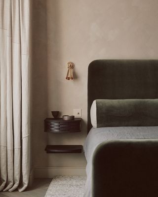 An olive green bed in velvet against a taupe wall