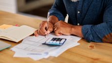 A man works on paperwork with a calculator, only his torso showing.