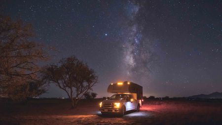 A small pickup RV is on a camping spot under the Milky Way
