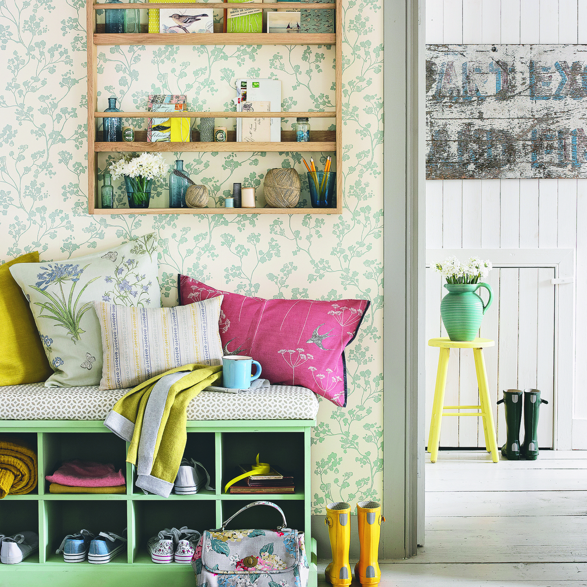 hallway wall decor ideas, bright and colourful hallway with bench seating, wall hung storage unit with vases, postcards, string, cushions, wellies, white floor boards, wallpaper