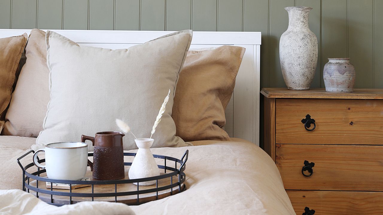 A bed with natural coloured bedding and a green panelled wall behind