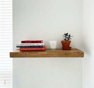 Wooden floating shelf styled with books, candle and small terracotta potted plant