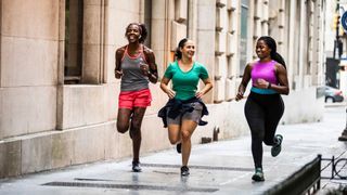 Three women running together in a line along the pavement after finding a running schedule